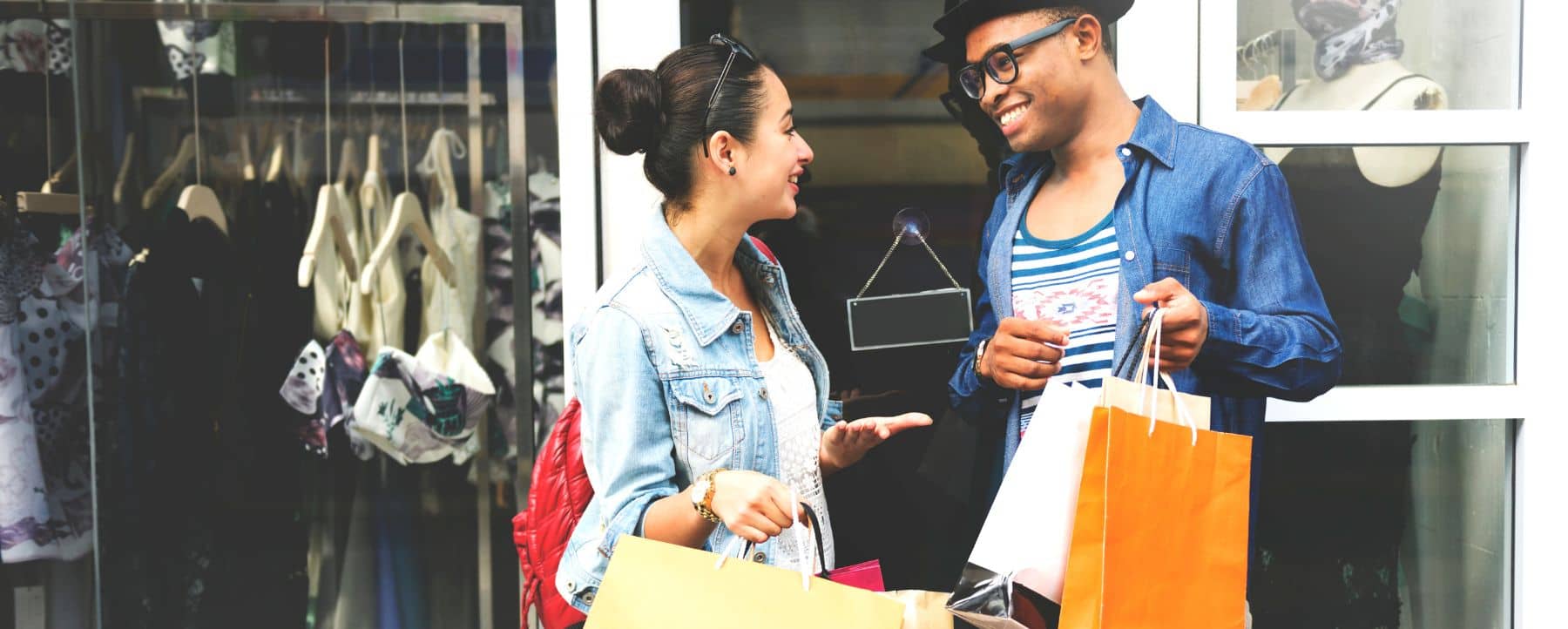 Two friends standing outside a shop, holding multicolored shopping bags and excitedly discussing a consumer promotion