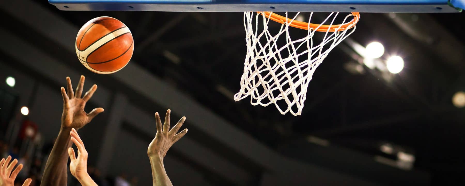 Close up of a basketball hoop and multiple hands reaching for an airborne basketball